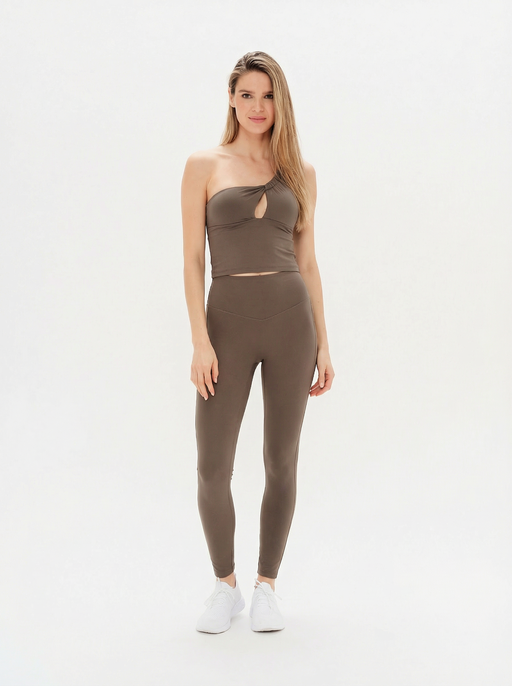 Woman wearing a brown one-shoulder top and leggings on a white background