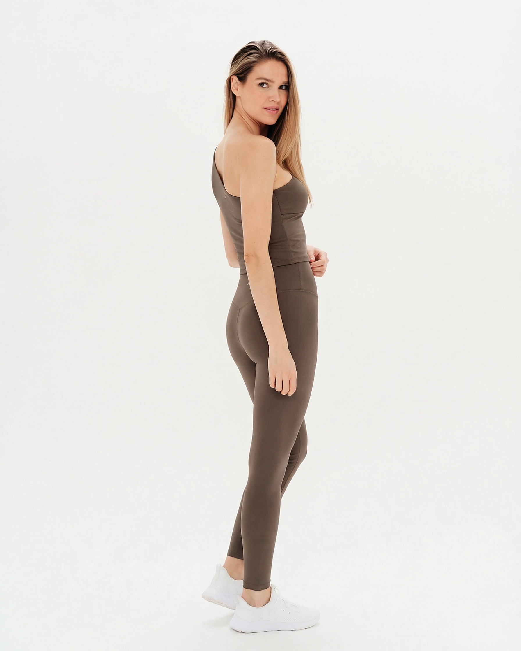 Woman wearing a brown sleeveless top and leggings on a white background