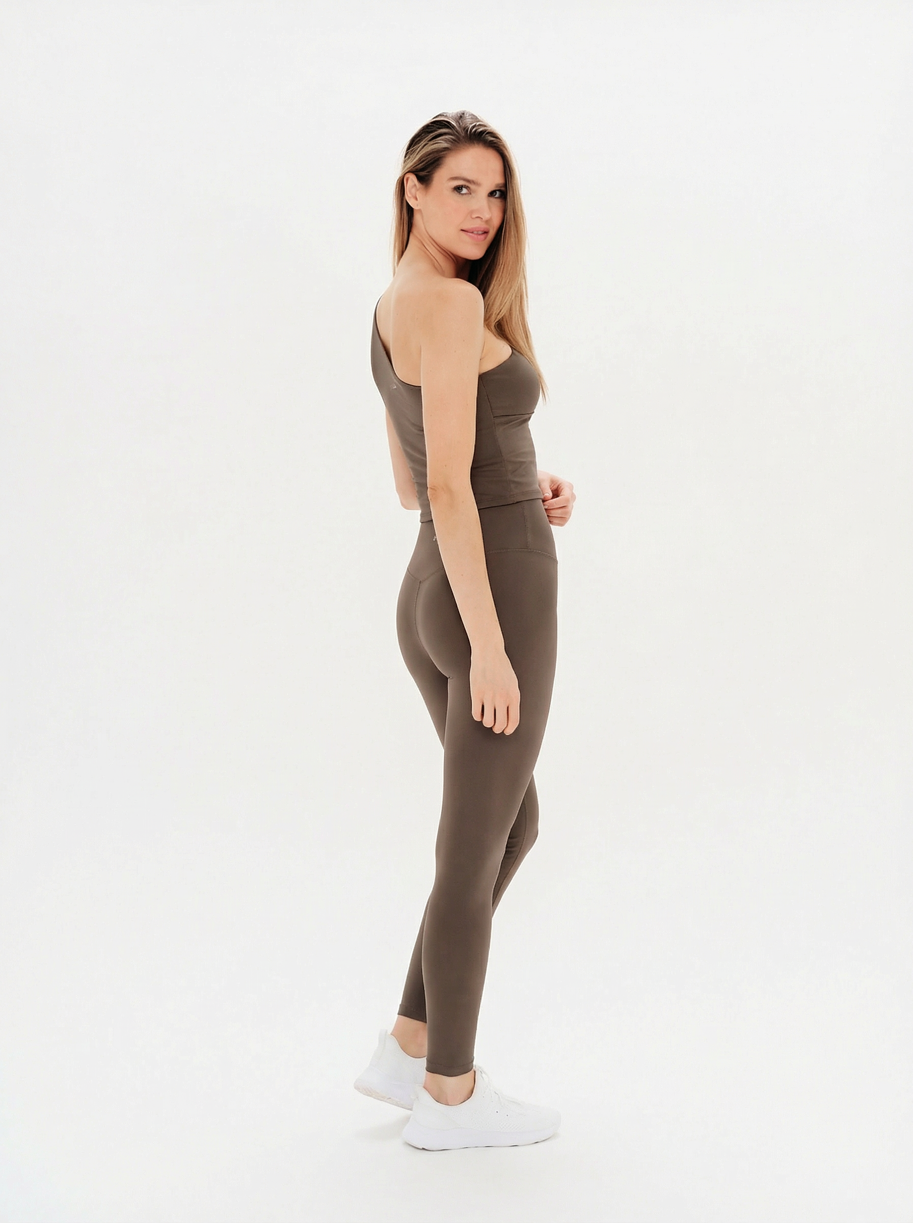 Woman wearing a brown sleeveless top and leggings on a white background